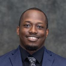 Professional headshot of a smiling Moemedi Rakhudu in a navy suit and patterned tie